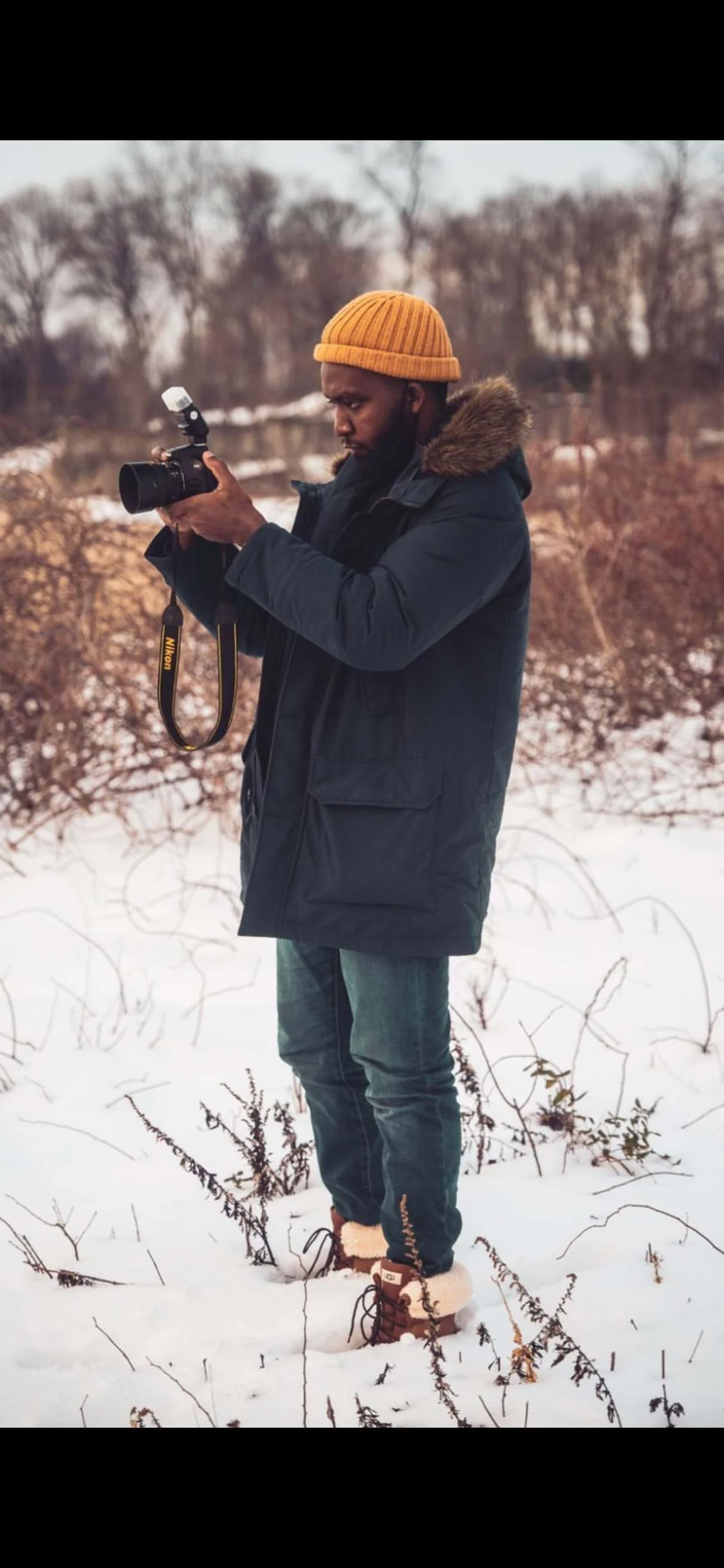 Dwight Robinson composing a shot on his Nikon in a snowy field, orange beanie and navy parka