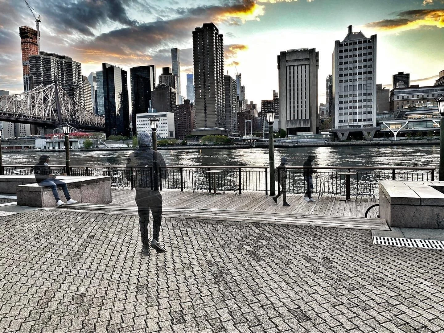Multiple-exposure figure walking a riverside promenade at sunset