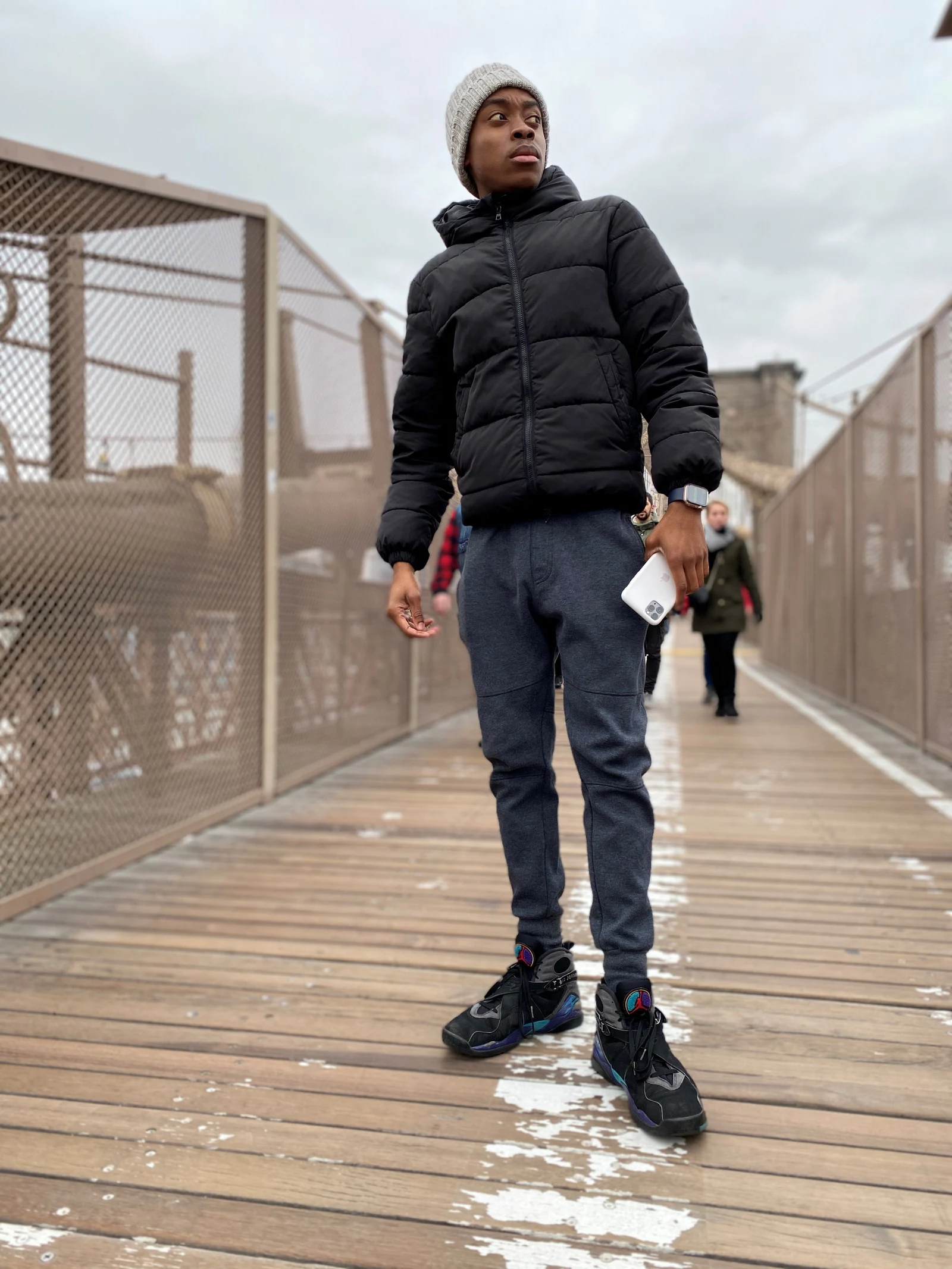 A young man in a winter jacket pausing on the Brooklyn Bridge walkway