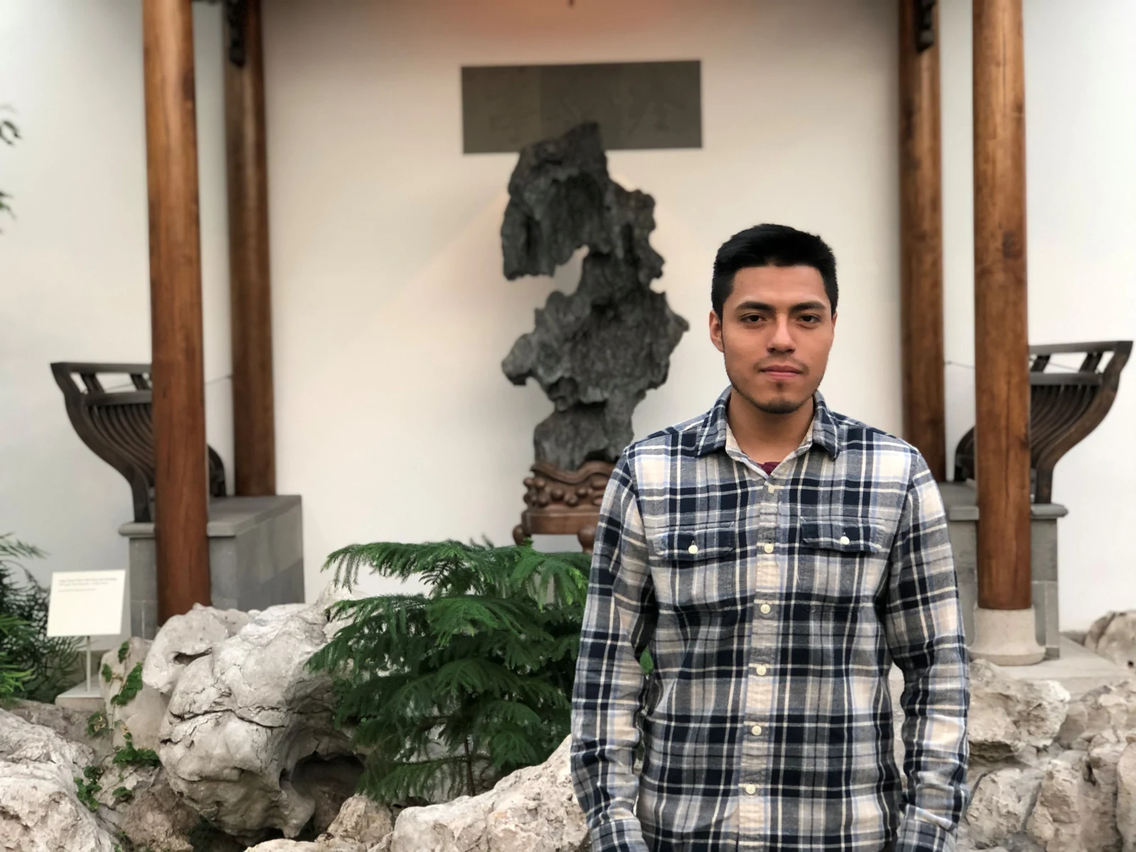 Man in a plaid shirt in a garden courtyard with a stone sculpture