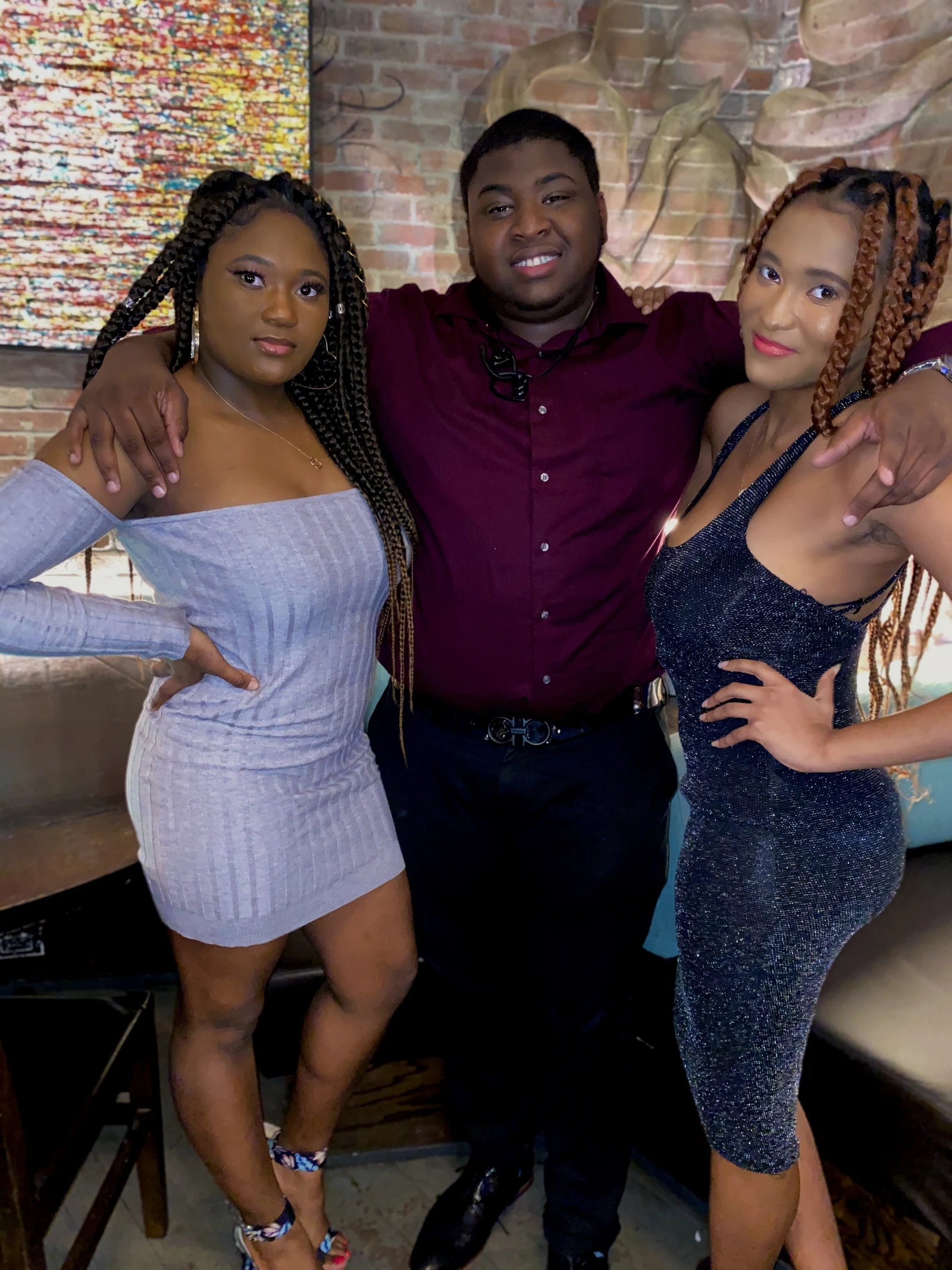 Three friends posing together at a brick-walled venue