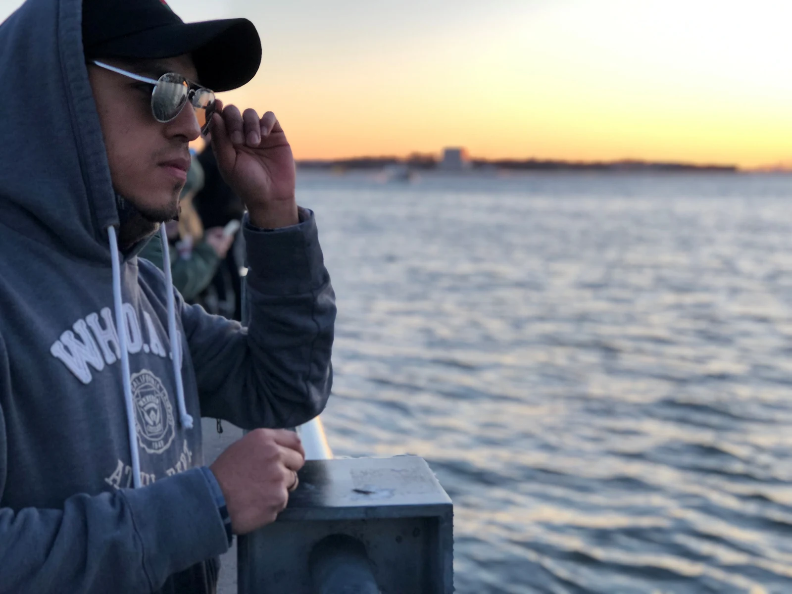 Man in sunglasses and a hoodie by the water at sunset