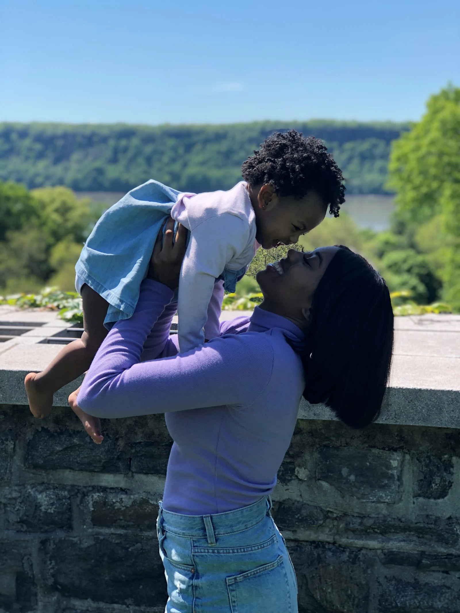 A mother lifting her child for a kiss at a stone overlook above the river