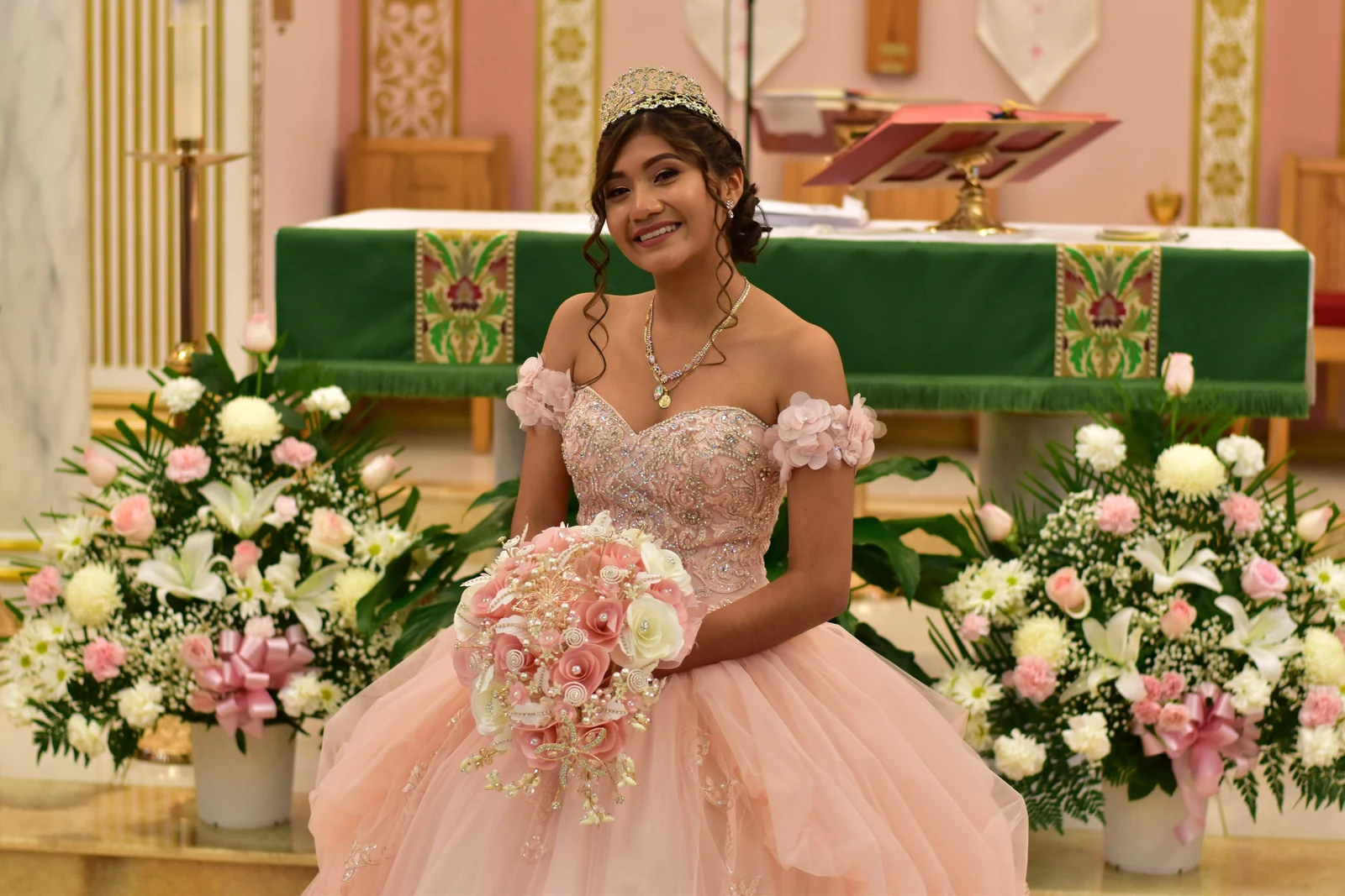 Quinceañera seated with her bouquet at the flower-lined church altar