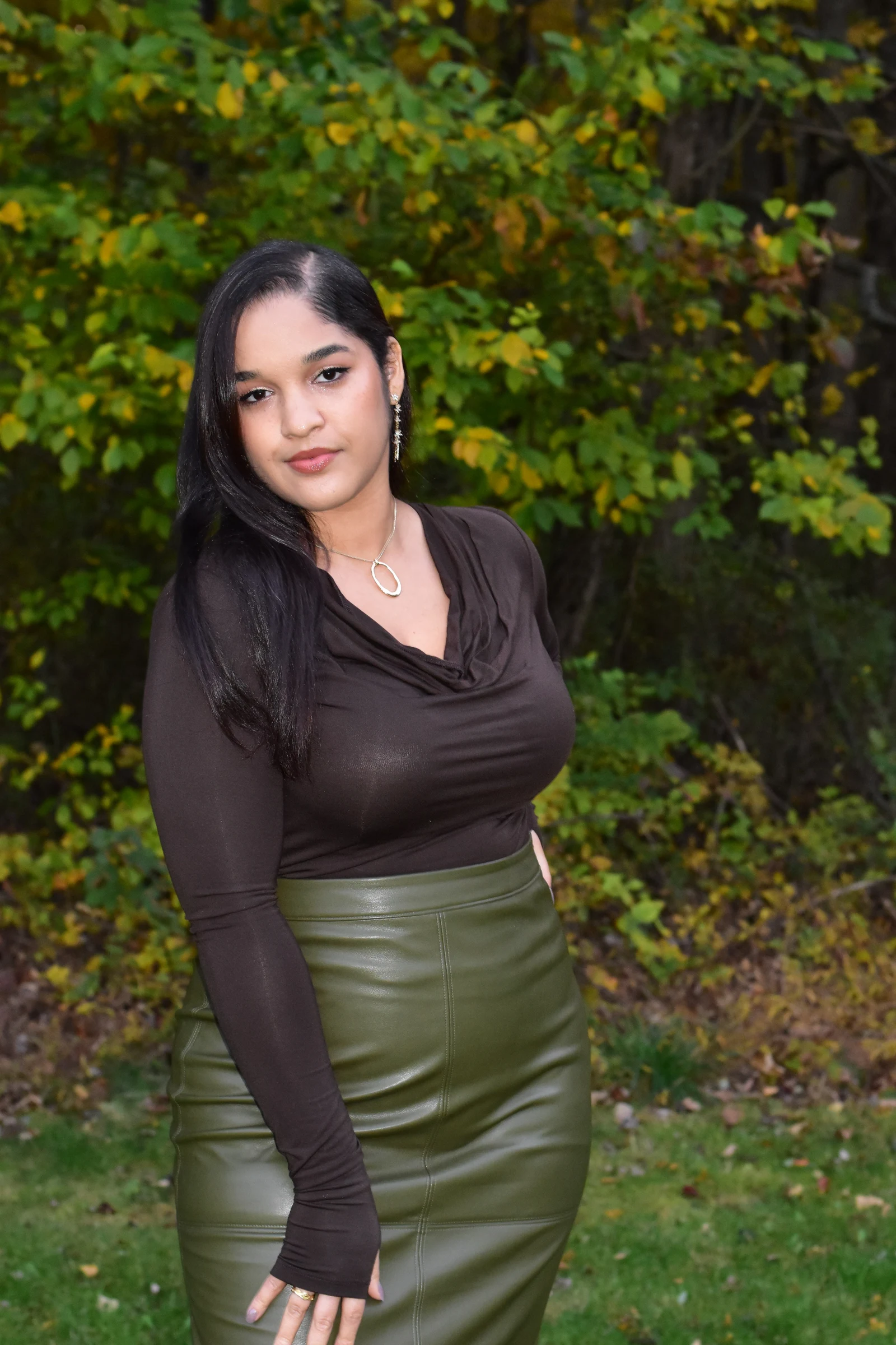 Autumn portrait of a woman in an olive skirt leaning into fall foliage