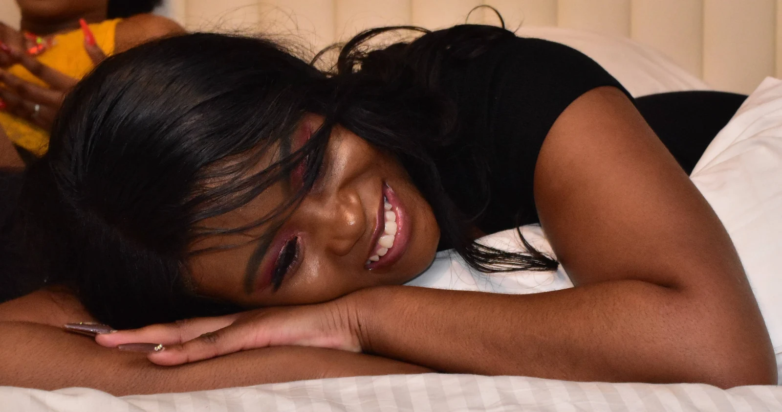 Portrait of a woman resting her head on her arms and smiling, on white bedding
