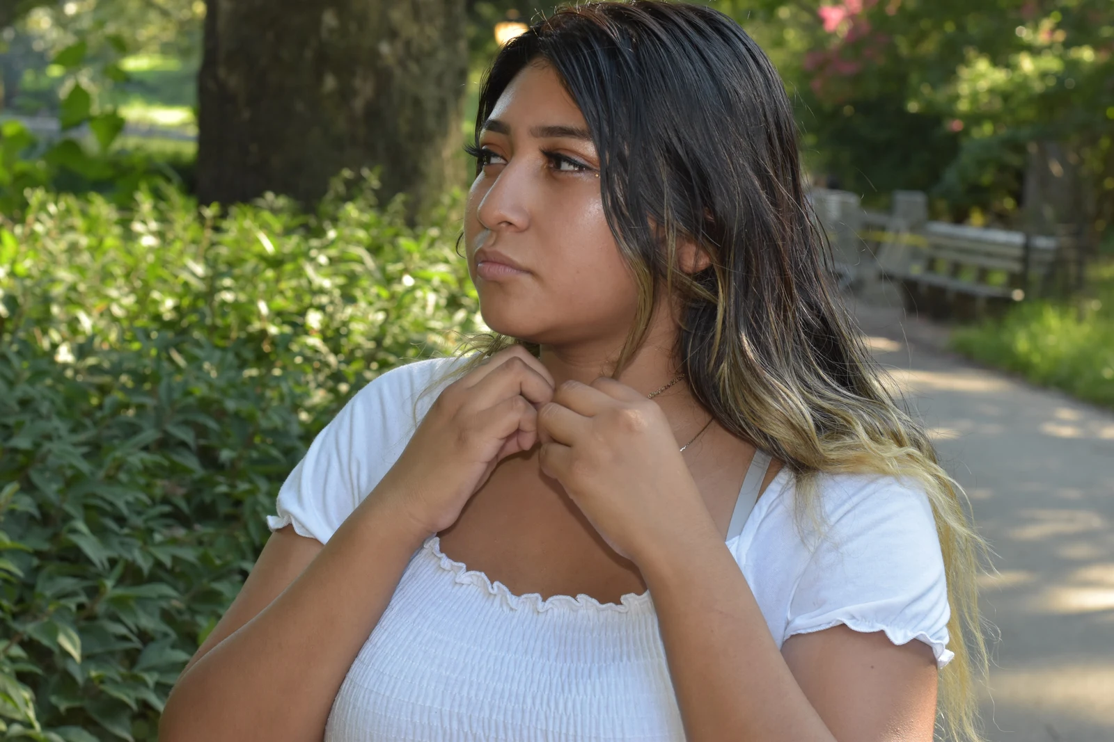 Summer portrait of a young woman in a white top on a shaded park path, looking off to the side