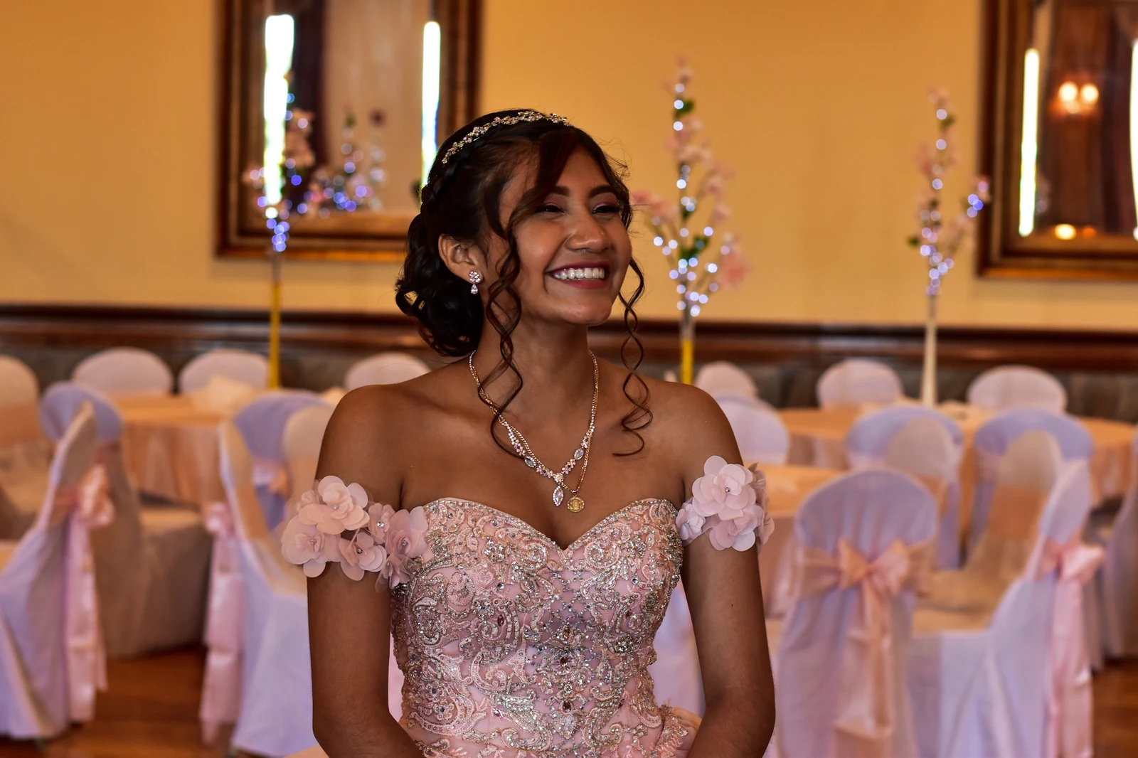 Quinceañera smiling in her gown in a decorated reception hall