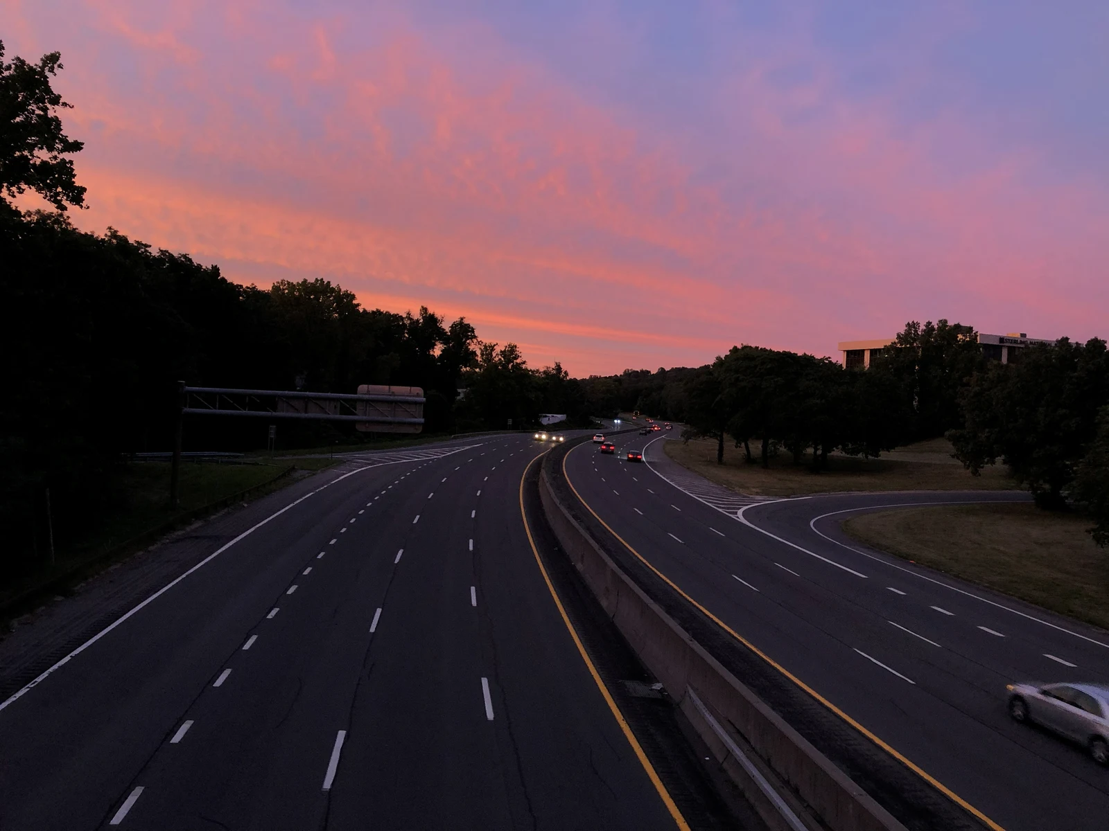 A highway curving through trees under a pink sunset sky