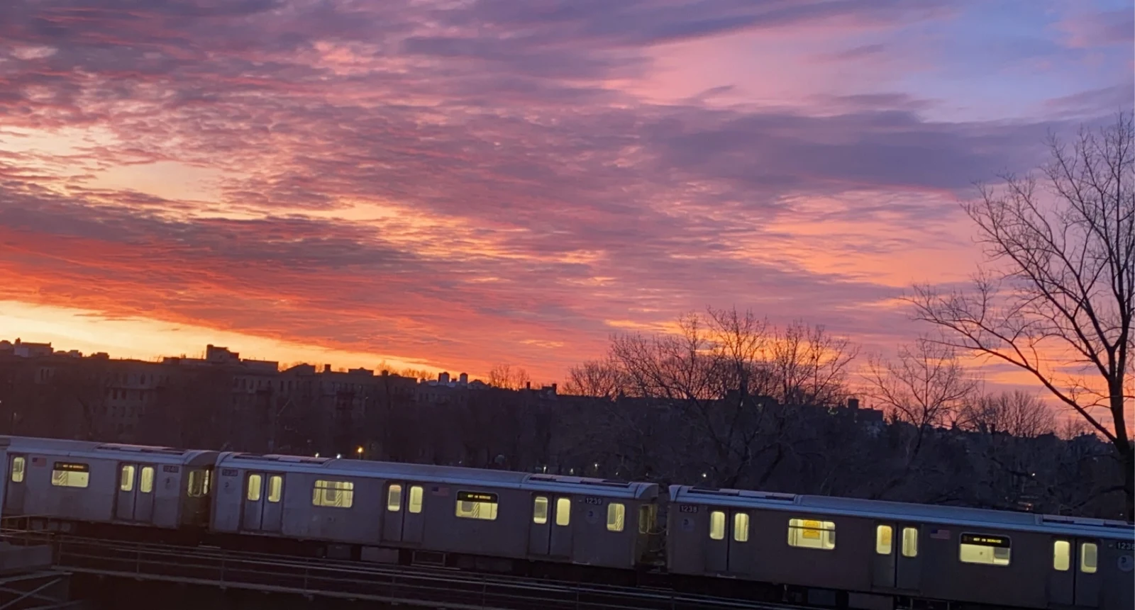 A subway train crossing an elevated track under a pink and violet sunset
